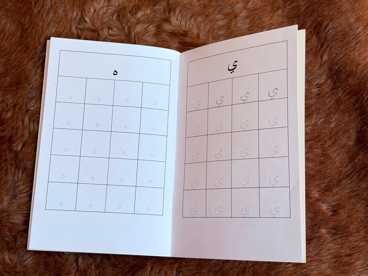 An open children's tracing workbook showing practice grids for writing numbers, placed on a brown faux fur surface.